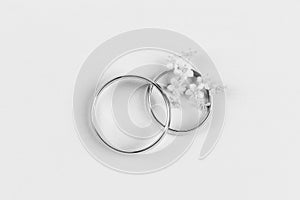 A pair of gold wedding rings and small white flowers in a ring on a white background