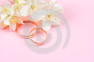 Pair of gold wedding rings and white Jasmine flowers on pink background