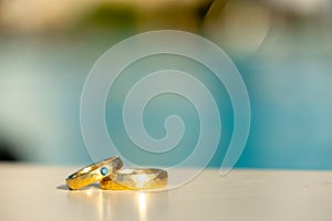 A pair of Golden Wedding Rings with Turquoise Diamond in Front of a Hotel Pool