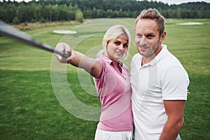 A pair of golfers make a photo on the golf course using a stick like a sephi pole