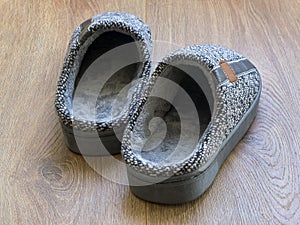 Pair of a gray mens house slippers on a brown wooden floor. Cozy, warm and comfortable domestic shoes