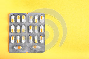 A pair of gray packagings of white and orange drugs in capsules. Painkillers on a yellow background. Healthful vitamins.