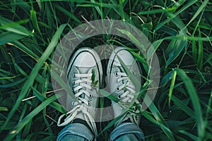 A pair of gray sneakers standing in a lush green grassy field. AIG51A photo