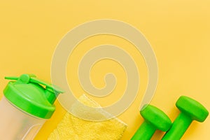 Pair of green dumbbells, towel and bottle of water on yellow background. Healthy lifestyle. Female fitness, slimming concept.