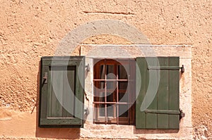 Pair of green, wood shutters, one open one closed, covering barred window, taly