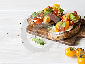 Pair of grilled toasts with cream cheese and slices of fresh tomatoes of various colors with fresh arugula and ground black pepper