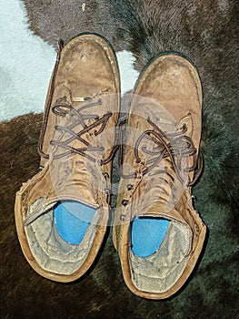 Pair of grungy mens boots with blue in-soles sitting on cowskin run - top view