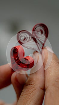 A pair of hands cradle a small, intricately crafted red paper heart