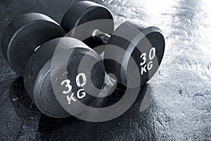 A pair of heavy 30 kilogram dumbbells on rubber floor matting at the gym. Made with cast iron and coated with rubber.