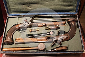 A pair of historic dueling pistols with accessories in an open case displayed in a museum.