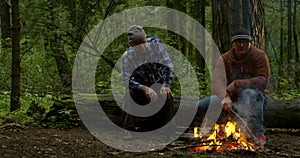 Pair of hunters are resting in woodland, burning fire and talking to each other