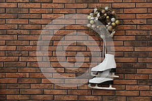 Pair of ice skates and beautiful Christmas wreath hanging on brick wall, space for text