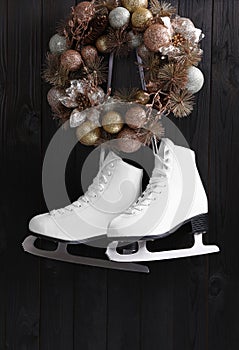 Pair of ice skates and beautiful Christmas wreath hanging on dark wooden wall