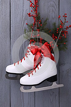 Pair of ice skates with Christmas decor hanging on grey wooden wall