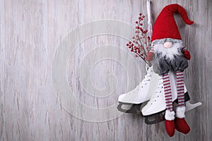 Pair of ice skates with Christmas gnome and decorative branches hanging on wooden wall, space for text