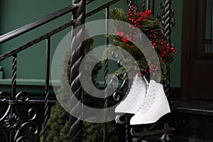 Pair of ice skates and Christmas wreath hanging on metal railing outdoors