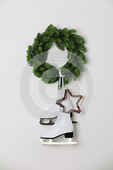 Pair of ice skates and Christmas wreath hanging on white wall