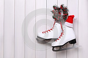 Pair of ice skates and Christmas wreath hanging on white wooden background, space for text