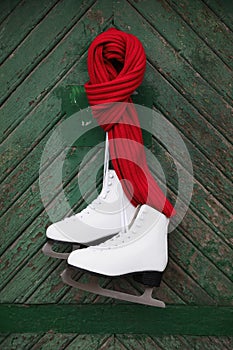 Pair of ice skates with knitted scarf hanging on green wooden wall