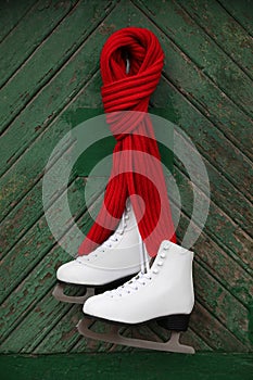 Pair of ice skates with knitted scarf hanging on green wooden wall