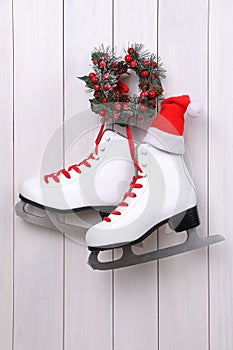 Pair of ice skates with Santa hat and Christmas wreath hanging on white wooden wall