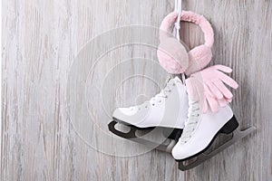 Pair of ice skates, warm earmuffs and gloves hanging on wooden wall, space for text