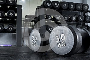 A pair of 30 kilo dumbbells on the floor with a dumbbell rack at the background. photo
