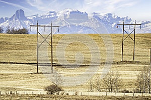 Pair of large wooden power poles with hanging electrical wires overlooking a hilltop and the distant Canadian Rocky Mountains near