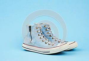 Pair of light blue worn textile sneakers with laces and zippers on a blue background