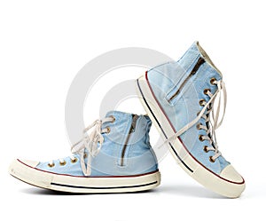 Pair of light blue worn textile sneakers with laces and zippers on a white background
