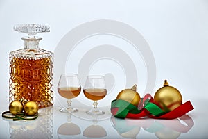 Pair of liquor glasses and bottle with Christmas ornaments, white backgrounds and reflections