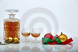 Pair of liquor glasses and bottle with Christmas ornaments, white backgrounds and reflections