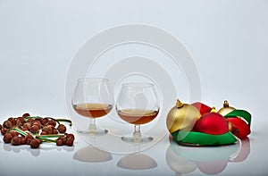 Pair of liquor glasses with Christmas ornaments and hazelnuts, white backgrounds and reflections