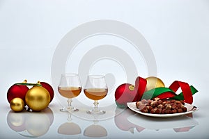 Pair of liquor glasses with Christmas ornaments and hazelnuts, white backgrounds and reflections