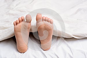 Pair of little girl`s feet in a bed