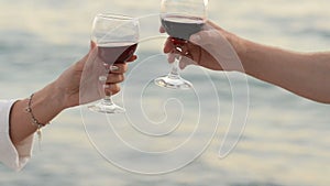 Pair of lovers clink glasses with red wine on the background of the sea