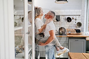 Pair of lovers kissing and hugging in kitchen next to the refrigerator