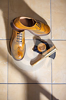 Pair of Luxury Male Full Brogued Tan Oxford Shoes. Placed Together with Shoe wax and Brush on Tiles Floor