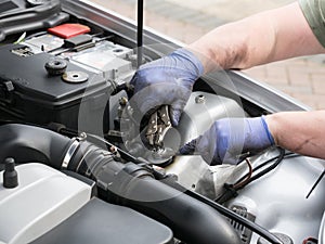 Pair of mechanic hands wearing blue gloves working in the engine bay of a sports car with plier grips and spanner