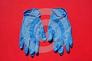 Pair of medical blue latex protective gloves on red background. Protective disposable gloves against the spread of virus, flu.