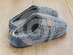 Pair of mens house slippers on a brown wooden floor. Cozy, warm and comfortable gray domestic shoes