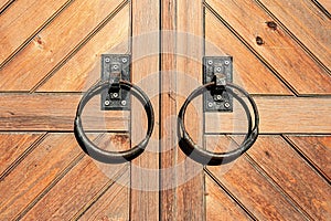 a pair of metal rings on a wooden door handle on a wooden door with a wooden plank pattern behind it