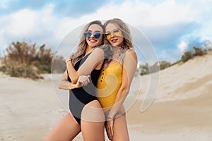 A pair of models in yellow and black swimsuit wearing sunglasses posing on the beach near the ocean. Couple of beautiful