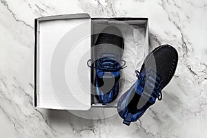 Pair of new mesh textile sneakers in the open box on a marble floor. Black blue fabric sneakers with laced fastening for active