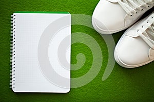 Pair of new stylish white sneakers on green background.
