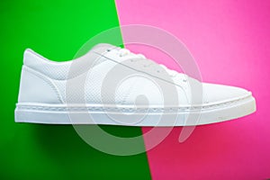 Pair of new stylish white sneakers on green pink background.