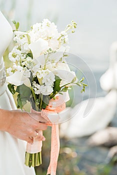 A pair of newlyweds with a bouquet of white roses sits near the lake. swan swims