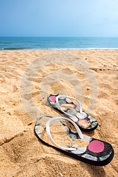 A pair och sandy flip flops on a beautiful summer beach.