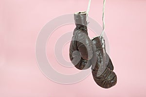 a pair of old boxing gloves hung in front of a candy-pink background