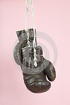 a pair of old boxing gloves hung in front of a candy-pink background